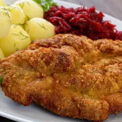 Kotlet schabowy w panierce z ziemniakami i buraczkami na białym talerzu.