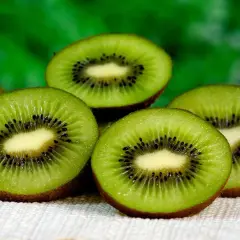 Kilka przekrojonych owoców kiwi z widocznymi czarnymi pestkami na jasnym tle.