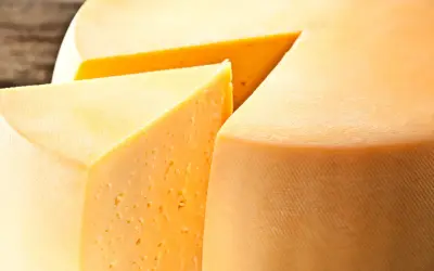 Kawałek sera Gouda z widocznymi oczkami i fragmentem całego kręgu sera.