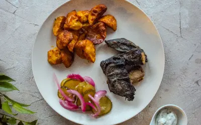 Talerz z pieczonymi ziemniakami, rybą i ogórkami kiszonymi.