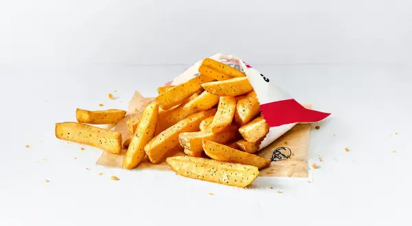 Stos małych frytek z KFC wysypany z papierowej torebki na białym tle.