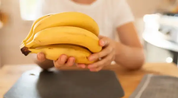 Dłoń trzymająca kiść żółtych bananów na drewnianym stole.