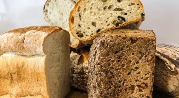 Różne rodzaje chleba, w tym bochenek z oliwkami i chleb żytni z ziarnami.