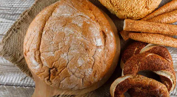 Różne rodzaje pieczywa: bochenek, paluszki sezamowe i obwarzanki.