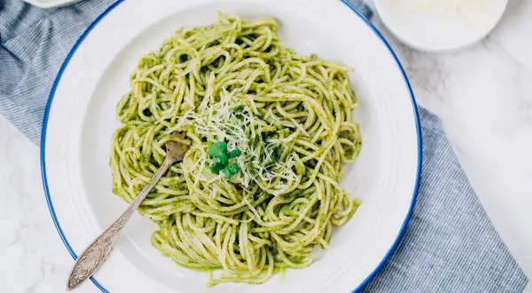 Porcja spaghetti z zielonym pesto, posypana parmezanem, na białym talerzu.