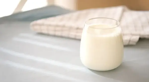 Szklanka mleka 2% na jasnym tle z tkaniną w kratkę.
