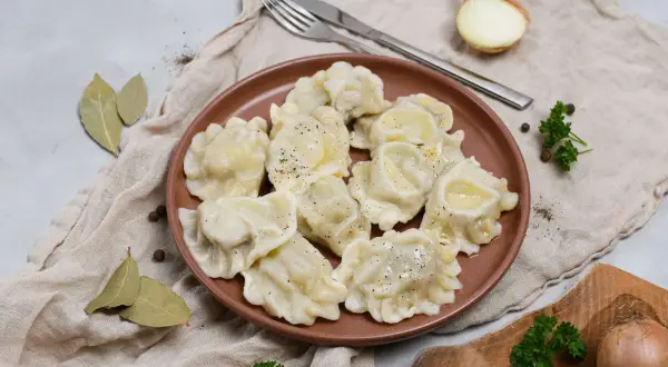 Smażone pierogi z mięsem na brązowym talerzu, z cebulą i natką pietruszki w tle.