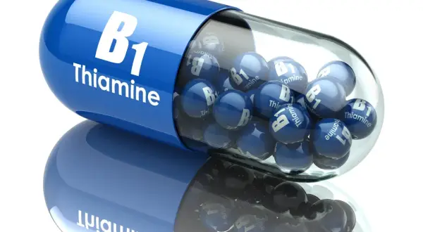 Niebieska kapsułka z napisem "B1 Thiamine" wypełniona małymi niebieskimi kulkami z tym samym napisem.