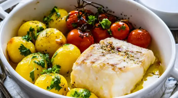 Pieczony filet rybny z ziemniakami i pomidorkami koktajlowymi w naczyniu żaroodpornym.